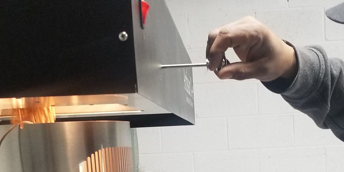 The roasting chamber of Gigawatt's fluid bed air roaster glowing mid-roast while a sample is pulled with the trier