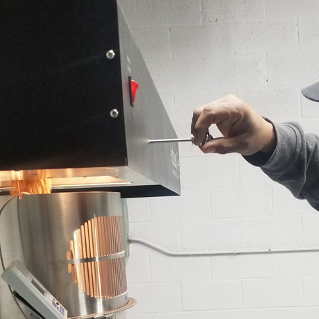 The roasting chamber of Gigawatt's fluid bed air roaster glowing mid-roast while a sample is pulled with the trier