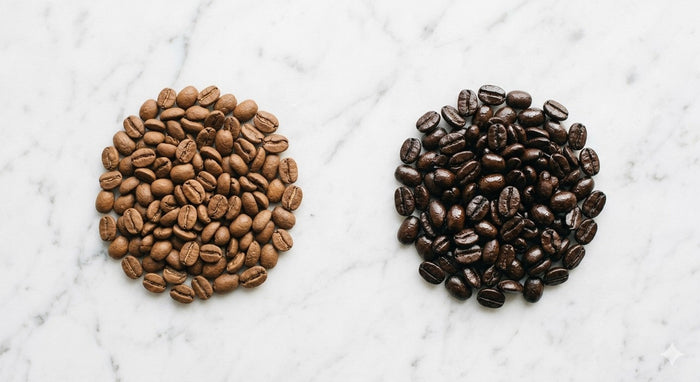 Light roast coffee beans next to dark roast coffee beans showing the color and texture difference between roast levels