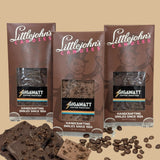 Coffee Chocolate Bar Collection 3-bar variety pack by Gigawatt Coffee Roasters and Littlejohn's Candies on a solid light brown background with chocolate and coffee beans on the surface